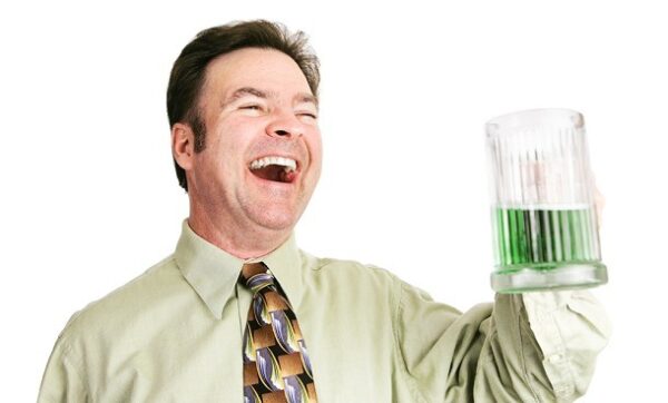 A lauging man holding a half full pint glass containing green liquid